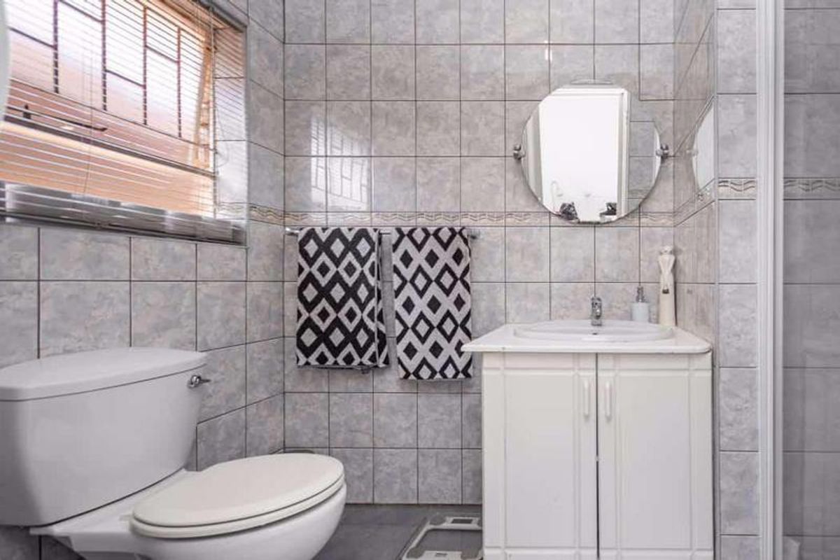 A functional bathroom featuring full-height ceramic wall tiling, a white vanity cabinet with integrated basin, and a standard toilet.