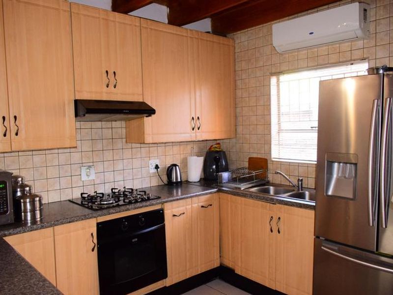 A functional kitchen featuring light wood cabinetry, granite countertops, a gas hob, built-in oven, and a tiled backsplash with an integrated air conditioning unit.