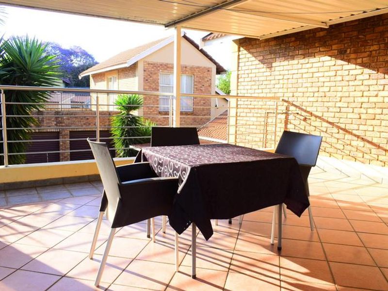A covered outdoor balcony featuring tiled flooring, an exposed brick wall, and metal safety railings, providing a functional space for outdoor relaxation.
