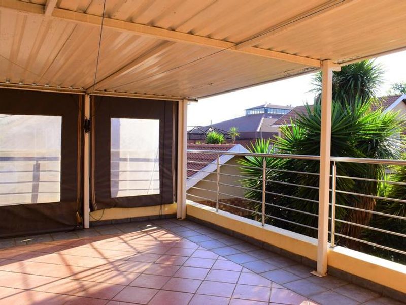A covered balcony featuring tiled flooring, a metal roof structure, and stainless steel balustrades, offering an open-air space suitable for outdoor relaxation.
