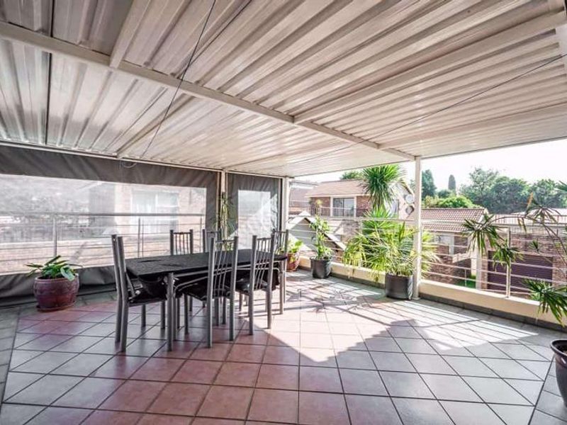A covered outdoor patio featuring tiled flooring, a corrugated metal roof, and protective canvas screens, offering a functional space for outdoor dining.