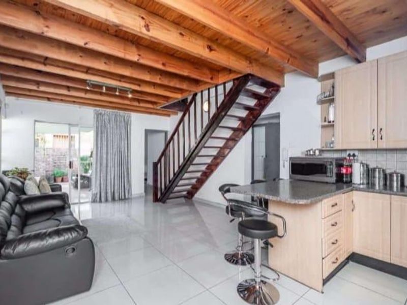 Open-plan living and kitchen area featuring exposed timber ceiling beams, tiled flooring, a timber staircase, and a functional kitchen with granite countertops.