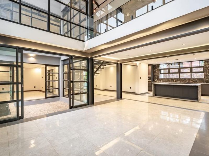 Spacious open-plan living area featuring high ceilings, modern kitchen with island, sleek steel-framed glass doors, and premium tiled flooring throughout.