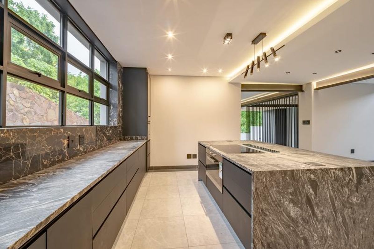 Modern kitchen featuring a large stone island, integrated induction cooktop, built-in oven, premium stone countertops, and sleek cabinetry with recessed and pendant lighting.