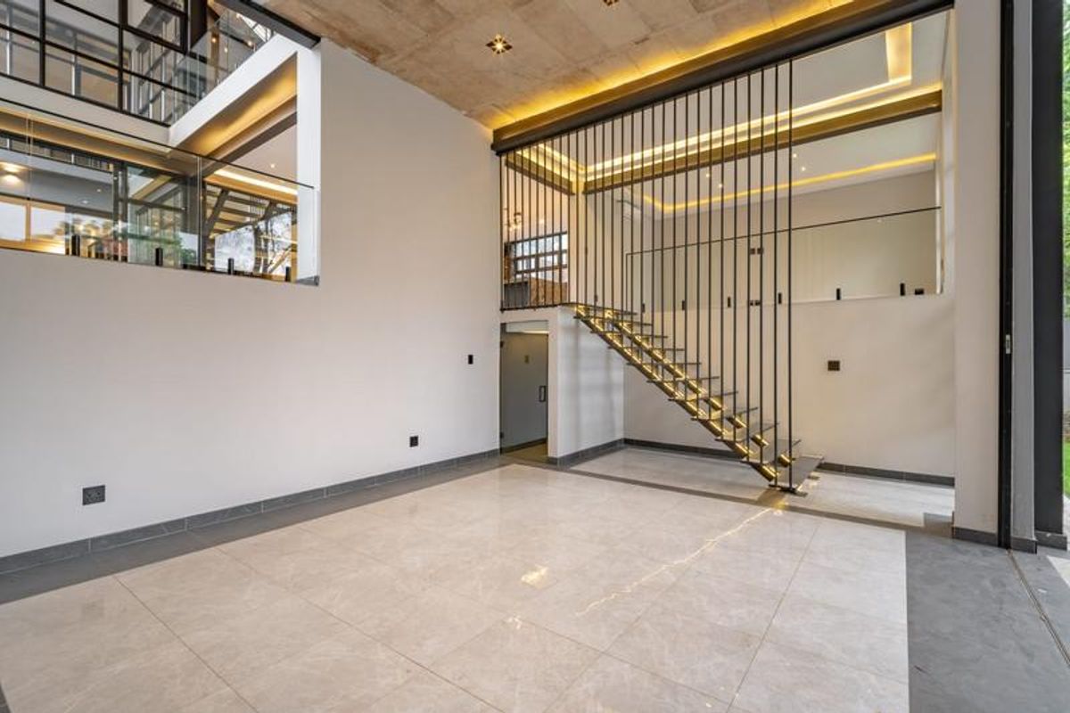 Spacious open-plan living area featuring a modern floating staircase, high ceilings with recessed lighting, and large glass panels overlooking the mezzanine level.