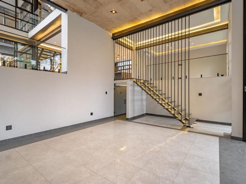 Spacious open-plan living area featuring a modern floating staircase, high ceilings with recessed lighting, and large glass panels overlooking the mezzanine level.