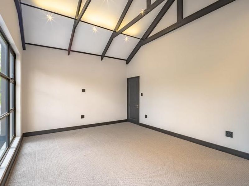 Spacious bedroom featuring a high vaulted ceiling with exposed timber beams, large grid windows, and neutral carpeted flooring.