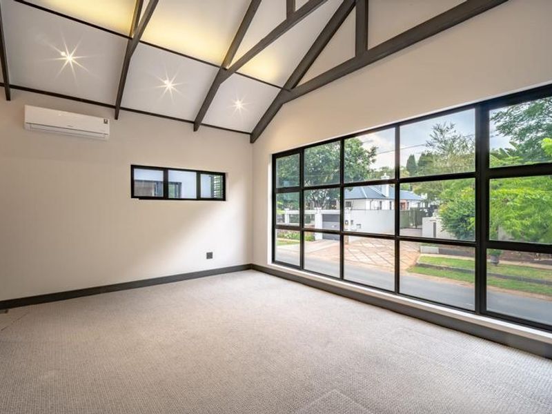 Bright and spacious living area featuring a high vaulted ceiling with exposed beams, large windows, and a modern split-system air conditioner.