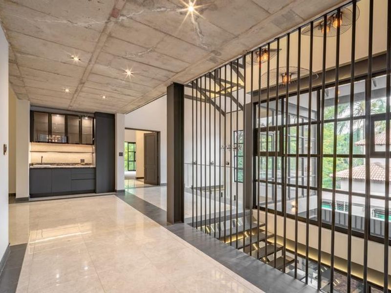 Modern hallway featuring an exposed concrete ceiling, sleek built-in kitchenette, and a striking metal staircase balustrade overlooking the lower level.