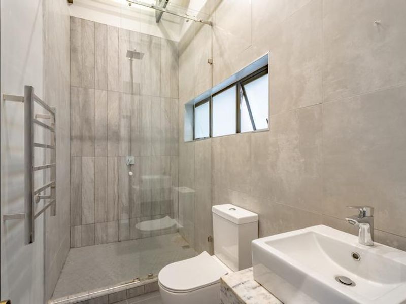 Modern bathroom featuring a walk-in shower with glass screen, rain shower head, heated towel rail, and a contemporary vanity basin.