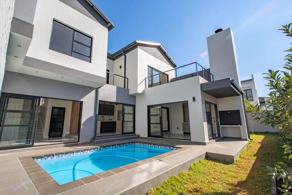 Modern rear exterior view featuring a swimming pool, tiled patio area, built-in braai, and large sliding glass doors leading into the home.
