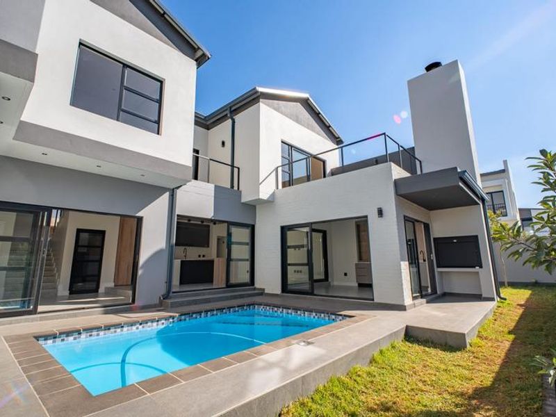 Modern rear exterior view featuring a swimming pool, tiled patio area, built-in braai, and large sliding glass doors leading into the home.