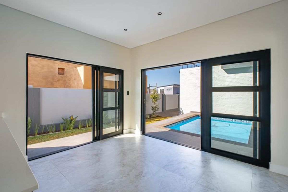 Bright, modern living area featuring large format floor tiles and expansive black aluminium sliding doors opening directly onto a private swimming pool and garden.