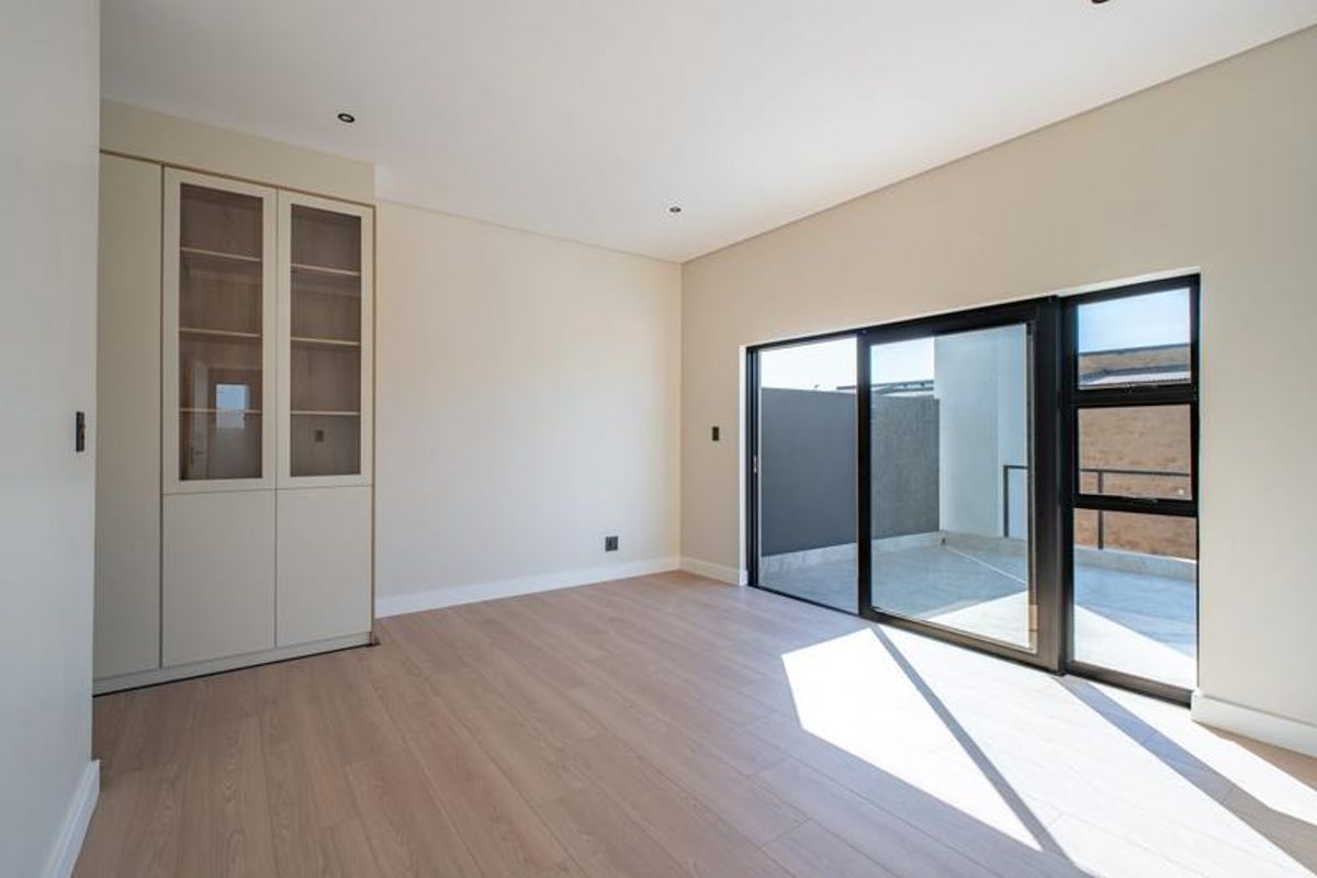 A bright, modern bedroom featuring light laminate flooring, built-in cabinetry, and a large sliding glass door providing access to an outdoor balcony.