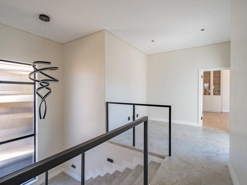 A modern, minimalist upper-level landing featuring sleek metal balustrades, large-format floor tiles, and a contemporary spiral pendant light fixture.