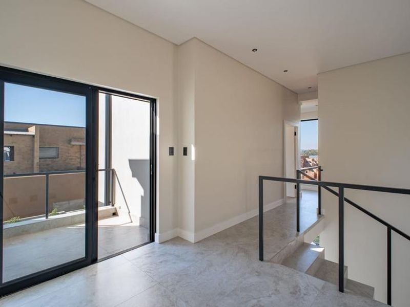 A bright, modern hallway featuring tiled flooring, a sleek metal staircase railing, and a sliding glass door leading to an outdoor balcony.