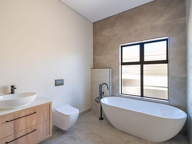 Modern bathroom featuring a sleek freestanding bathtub, wall-mounted toilet, and a contemporary vanity with a vessel sink and matte black fixtures.
