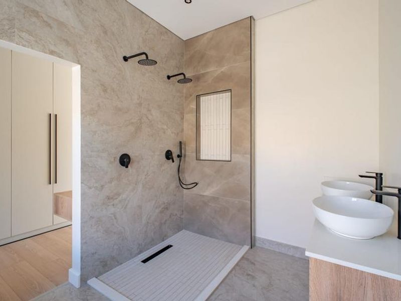 Modern bathroom featuring a spacious walk-in shower with dual shower heads, stone wall tiling, and a double vanity with matte black fixtures.