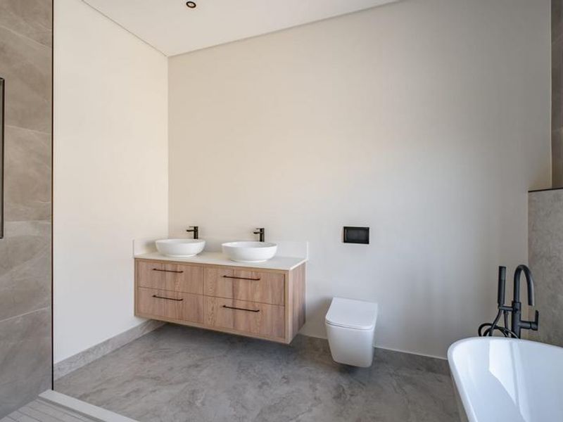 Modern bathroom featuring a floating double vanity, wall-mounted toilet, freestanding bathtub, and contemporary black matte fixtures with neutral large-format tiling.