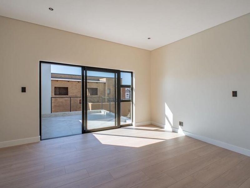 A bright, empty bedroom featuring modern laminate flooring, recessed lighting, and a large sliding glass door providing access to an outdoor balcony.