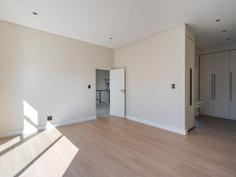 A bright, modern bedroom featuring neutral walls, light laminate flooring, recessed downlights, and ample built-in cupboard storage.