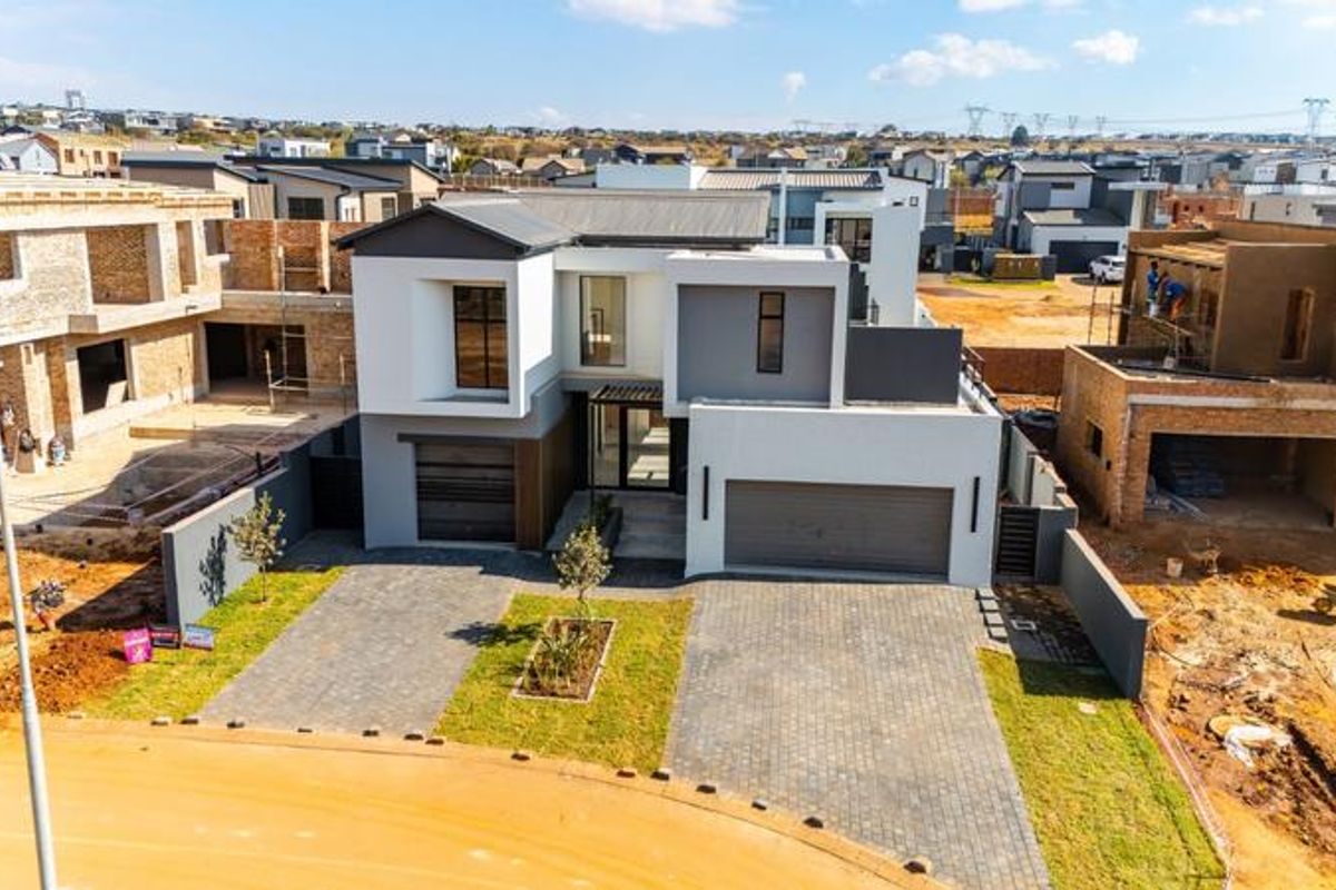 Aerial view of a modern double-story residential property featuring a paved driveway, double garage, and established boundary walls in a developing estate.