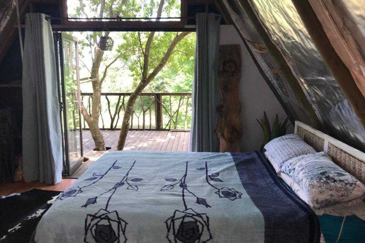 A rustic A-frame bedroom featuring exposed structural beams, sloped ceilings, and bi-fold doors opening onto a private timber deck nestled among trees.