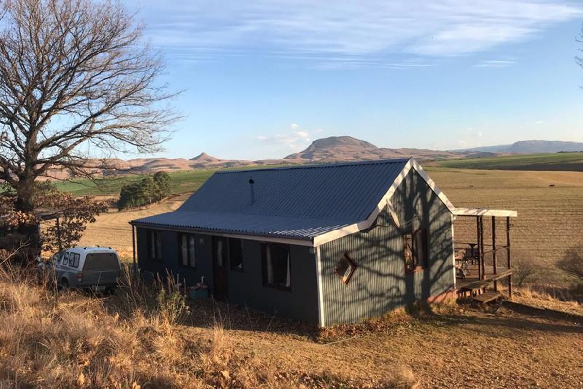 A rural cottage featuring corrugated metal cladding and a timber deck, set against a scenic landscape with mountain views.
