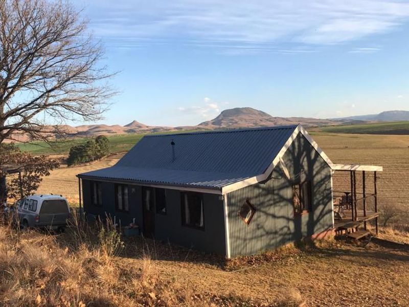 A rural cottage featuring corrugated metal cladding and a timber deck, set against a scenic landscape with mountain views.