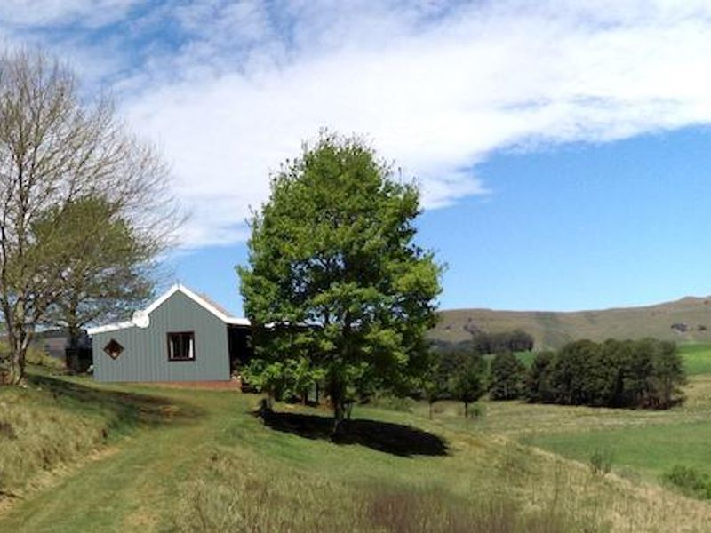 A view of the rear elevation of the farm dwelling, featuring metal cladding and a pitched roof set against a scenic rural landscape.
