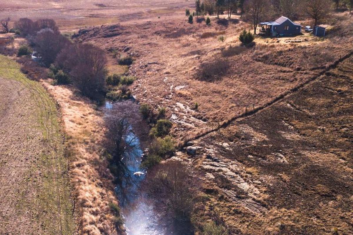 Aerial view of a rural farm property featuring a natural stream running through the landscape with a small dwelling situated on the hillside.