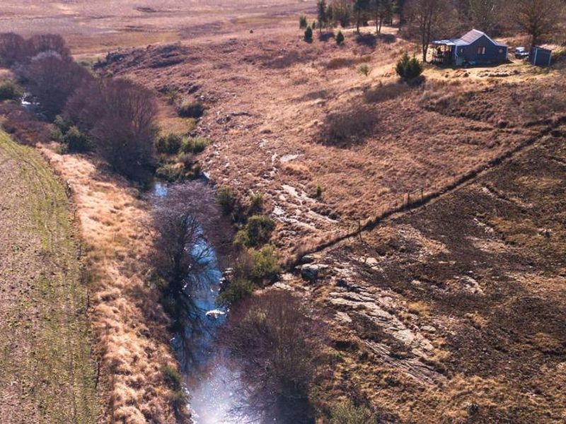 Aerial view of a rural farm property featuring a natural stream running through the landscape with a small dwelling situated on the hillside.