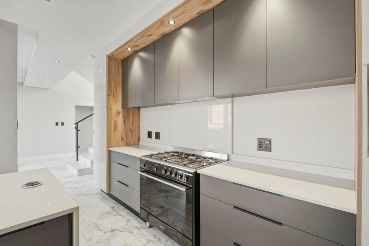 Modern kitchen featuring sleek grey cabinetry, wood-accented shelving, stone countertops, a gas stove, and elegant marble flooring.