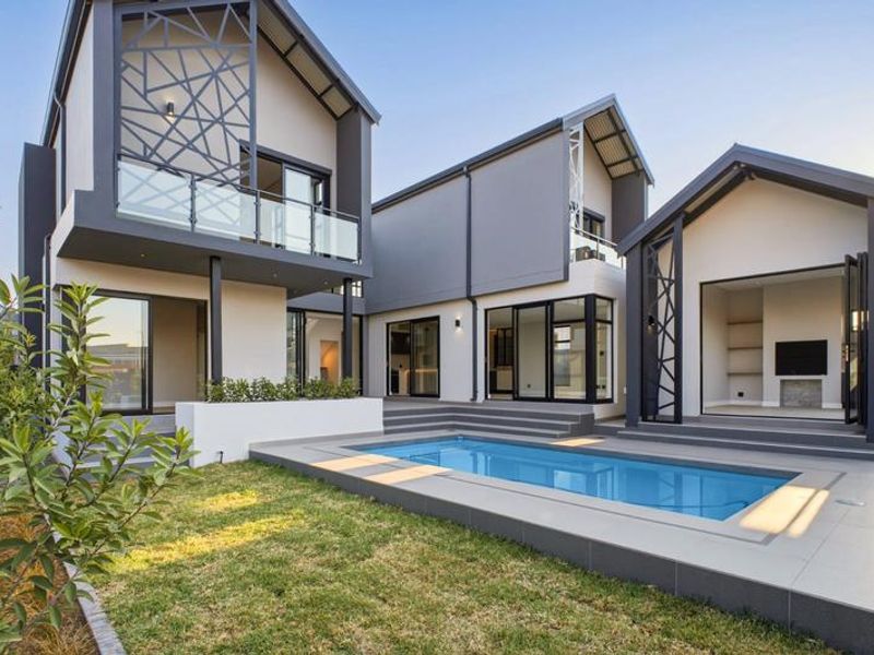 Modern rear exterior featuring a swimming pool, tiled deck, contemporary architectural design with glass balustrades, and seamless indoor-outdoor flow through large sliding doors.
