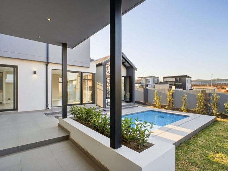 Modern covered patio area featuring tiled flooring, recessed lighting, and direct access to a private swimming pool and landscaped garden.