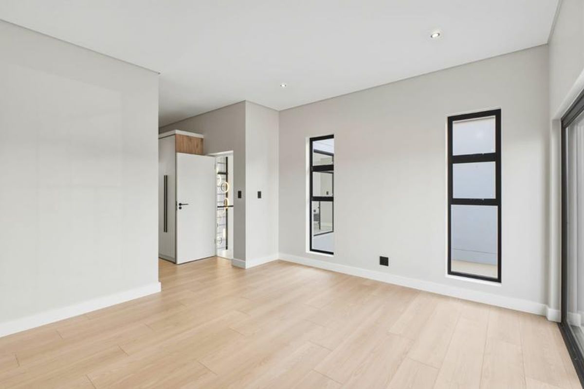 A bright, modern, and empty living area featuring light wood-look laminate flooring, neutral walls, and contemporary black-framed windows.