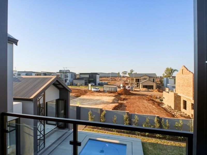 Elevated balcony view overlooking a modern residential estate with a private swimming pool and surrounding construction.