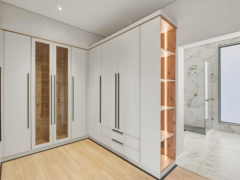 Modern dressing area featuring extensive built-in cabinetry with integrated shelving and lighting, leading into a contemporary bathroom with marble-look finishes.