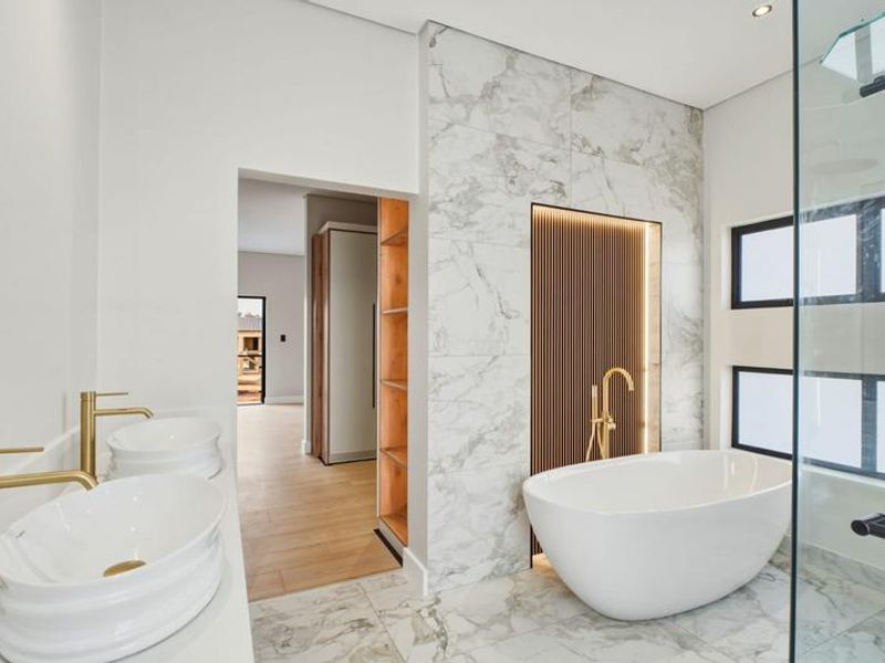 Modern luxury bathroom featuring a freestanding bathtub, double vanity with brass fixtures, marble-look tiling, and a stylish slatted wood accent wall.