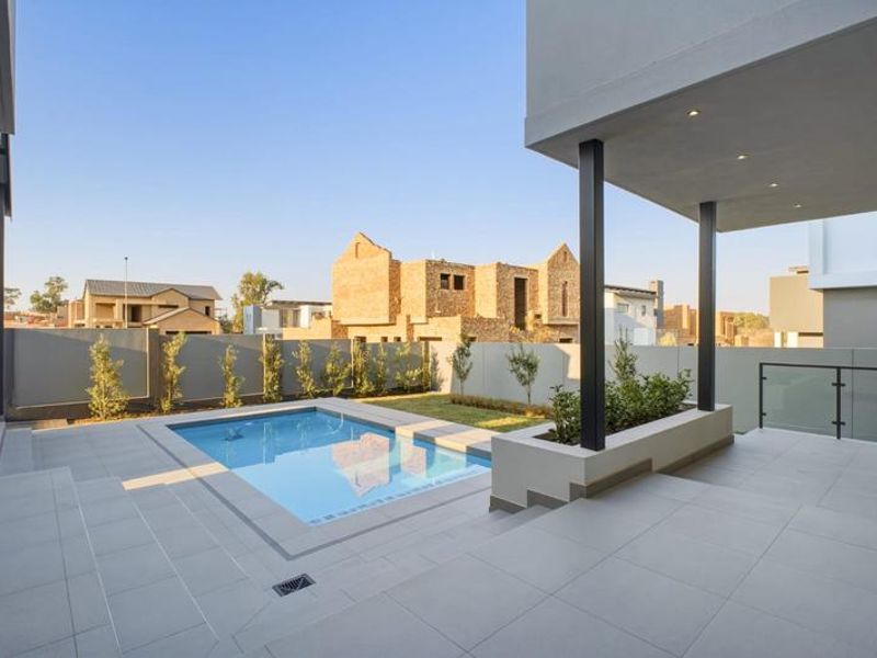 Modern outdoor living area featuring a sleek swimming pool, tiled patio, raised planter box, and glass balustrade, perfect for entertaining.