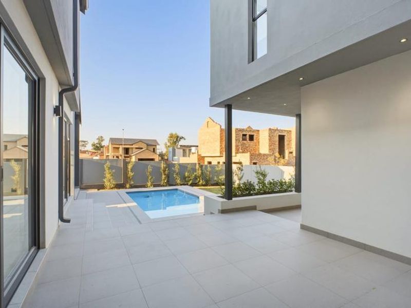 A modern covered patio area featuring large format floor tiles, recessed lighting, and direct access to a private swimming pool.