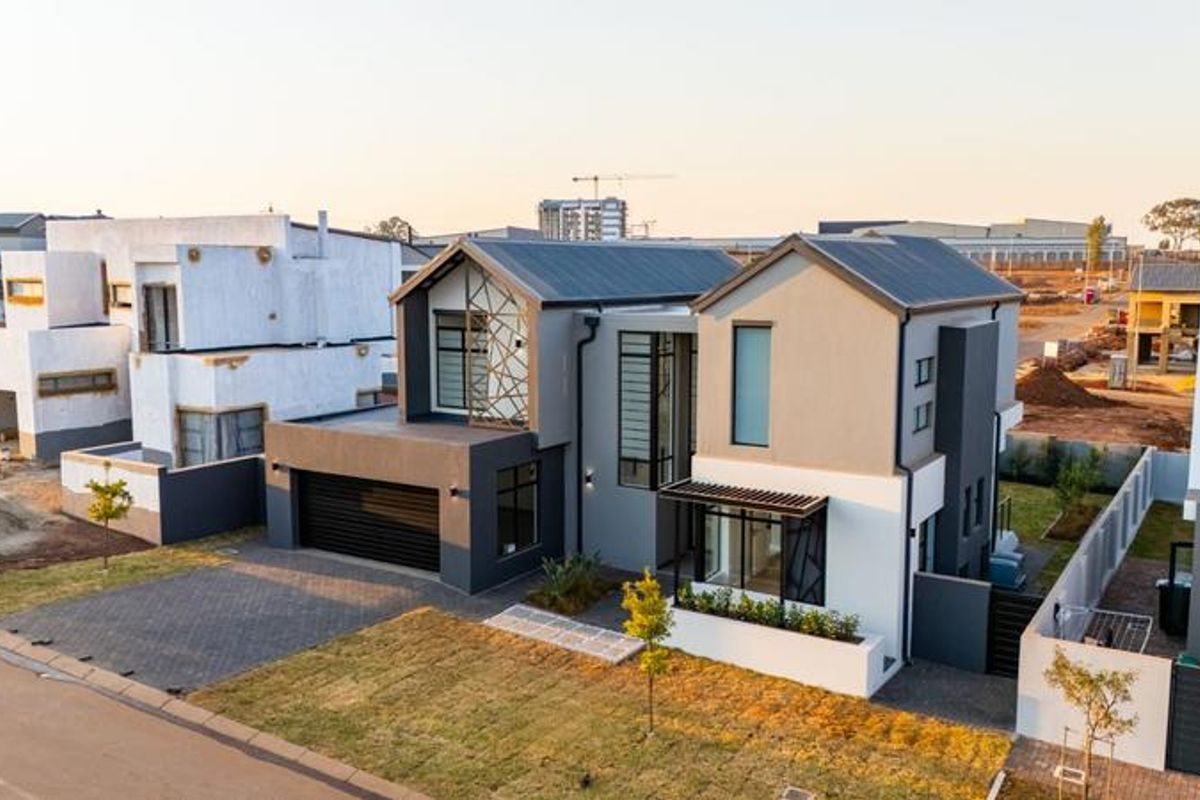 Aerial view of a modern double-story residential home featuring a metal roof, paved driveway, and contemporary architectural design in a developing estate.
