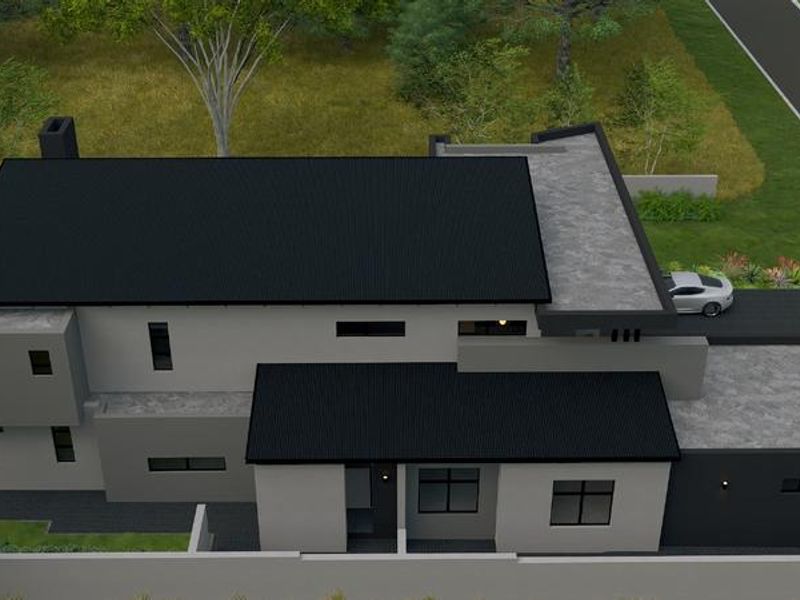 Aerial view of a modern residential property featuring a combination of pitched corrugated metal and flat concrete roofing with a paved driveway.