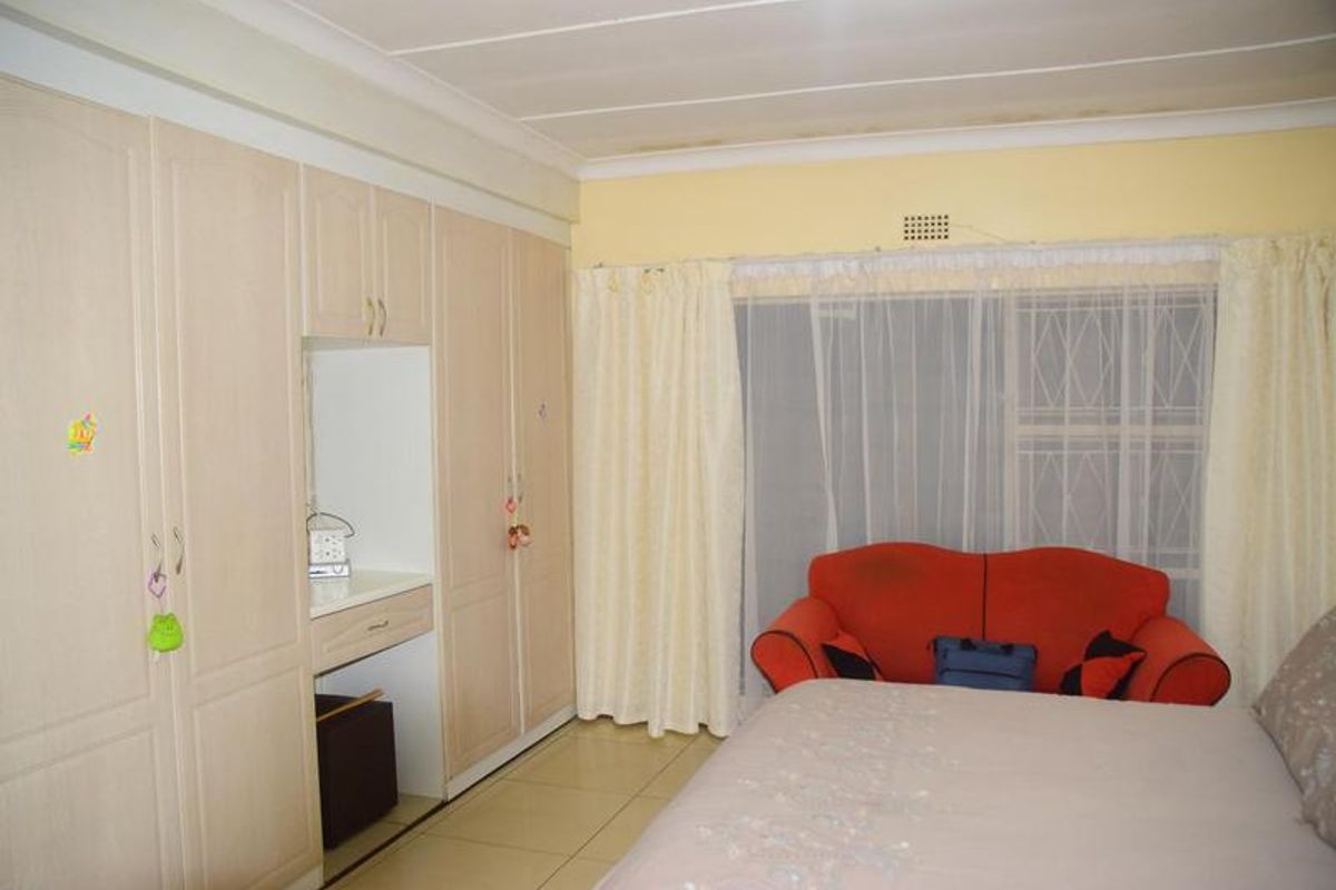 A bedroom featuring built-in cupboards, tiled flooring, and a security gate on the window. Note visible water staining on the ceiling.