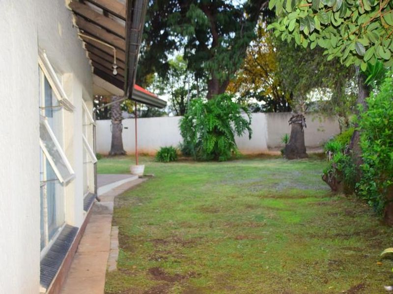 A view of the rear garden featuring a lawn area, perimeter boundary wall, and the side elevation of the house with casement windows.