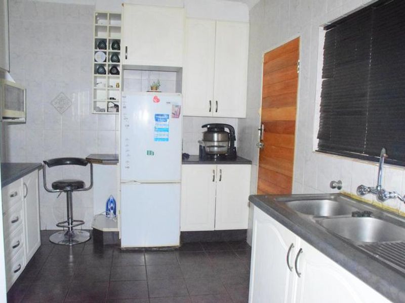 A functional kitchen featuring white built-in cabinetry, a double stainless steel sink, and tiled surfaces throughout.