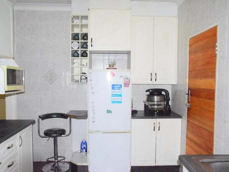 A functional kitchen featuring white built-in cabinetry, tiled wall splashbacks, and laminate countertops, providing a practical workspace with integrated storage and appliance housing.