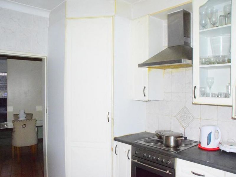 A functional kitchen featuring white cabinetry, a built-in electric stove, stainless steel extractor fan, and tiled backsplash.