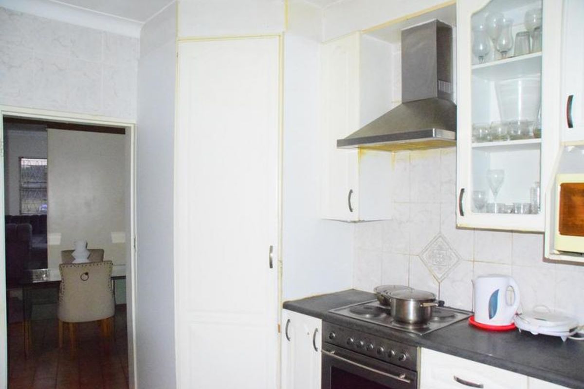 A functional kitchen featuring white cabinetry, a built-in electric stove, stainless steel extractor fan, and tiled backsplash.
