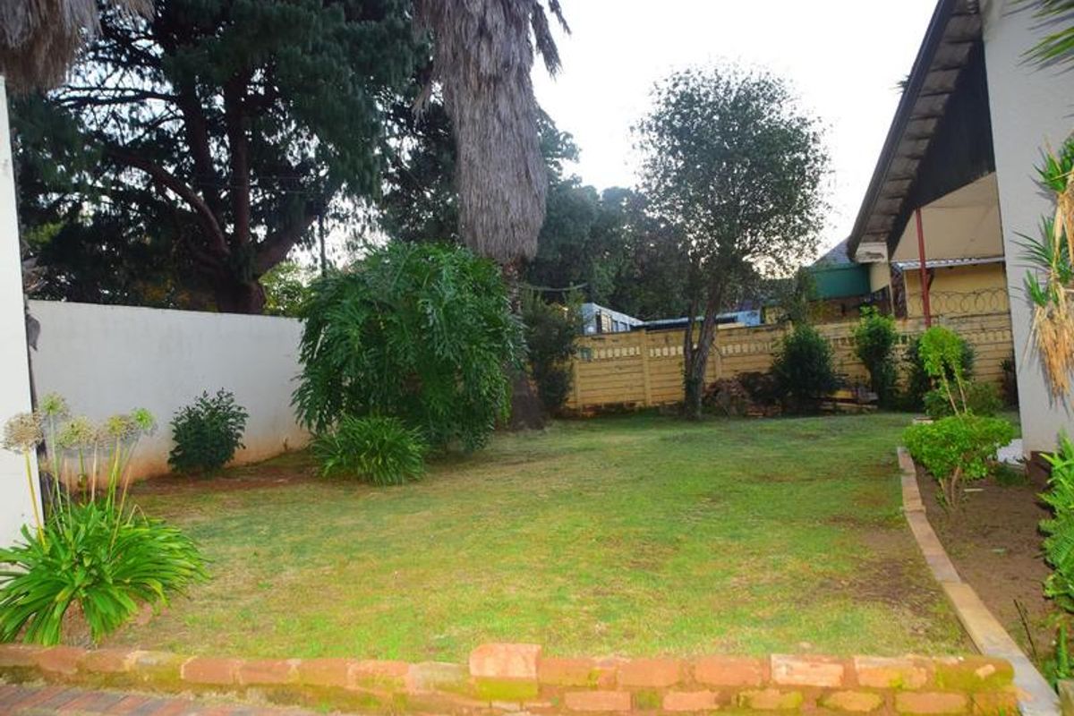 A private rear garden featuring a lawn area, established trees, and perimeter boundary walls with brick edging.